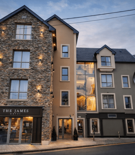 Charming boutique hotel with lit stone façade, modern glass atrium, inviting exterior at dusk in scenic town.